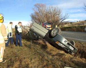 Emergency staff inspect the wreckage of a car which hit black ice and rolled on State Highway 85...