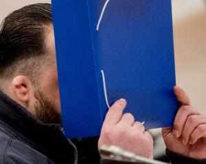 Former nurse Niels Hoegel covers his face as he arrives for the start of his trial in a courtroom...