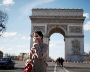 A woman wearing a protective mask, walks near Arc de Triomphe as France grapples with an outbreak...