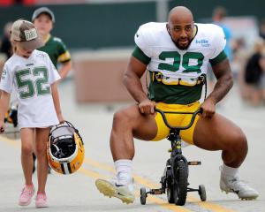 A young fan watches as Green Bay Packers running back AJ Dillon tries his best to ride her bike...