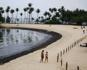 People walk next to an oil slick at Tanjong Beach on Sentosa, Singapore. Photo: Reuters