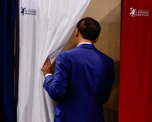French President Emmanuel Macron heads into the voting booth during France’s first round of...