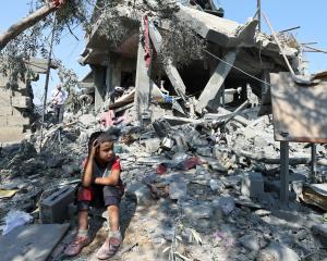 A child sits amid the rubble as Palestinians inspect a house destroyed in an Israeli strike in...