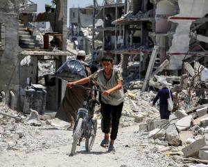 A Palestinian youth pushes a bicycle as he walks past the rubble of houses destroyed during the...