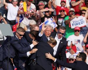 Donald Trump gestures with a bloodied face while he helped off stage after an assassination...