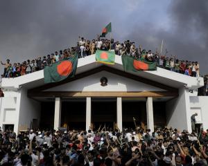 Anti-government protesters display Bangladesh’s national flag as they storm former prime minister...