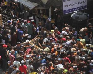 Palestinians gather to receive food cooked by a charity kitchen, near the ruins of houses...