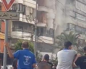 People watch as smoke rises from a building following an explosion, as hand-held radios used by...