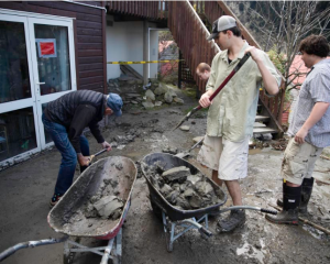 Jasper Thompson, middle right, shovels debris into a wheelbarrow as residents of Reavers Lane,...