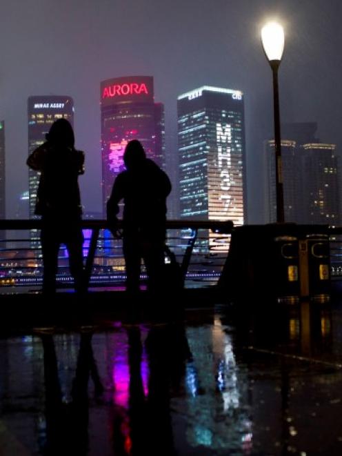 People on the Bund look at a building with lights forming the words MH370, the flight number of...