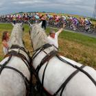 A pack of riders cycles past spectators with horses during the fifth stage of the 99th Tour de...