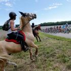 Horse riders watch as the pack of riders cycles on its way during the 187.5km 11th stage of the...