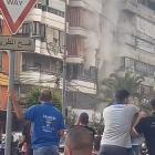 People watch as smoke rises from a building following an explosion, as hand-held radios used by...