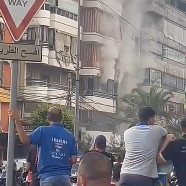 People watch as smoke rises from a building following an explosion, as hand-held radios used by...