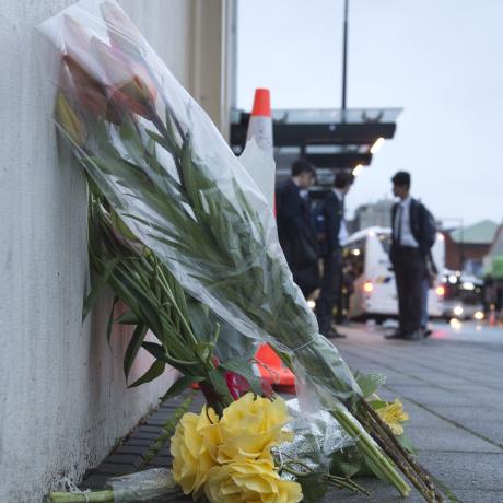 High school pupils wait for their bus this morning beside flowers placed at the scene of...