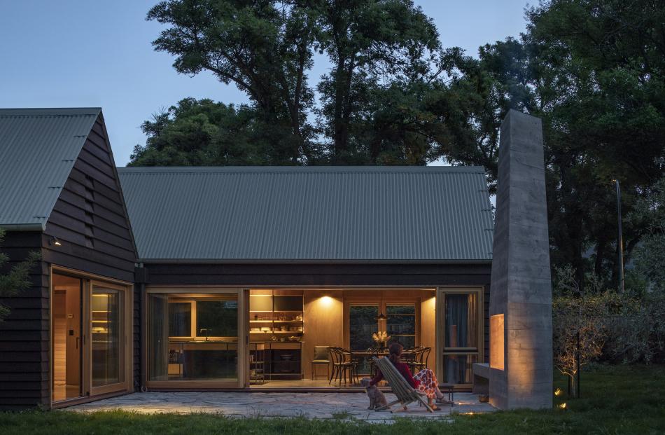 The tall chimney of the outdoor fire contrasts with the home’s horizontal lines. The owners plan...