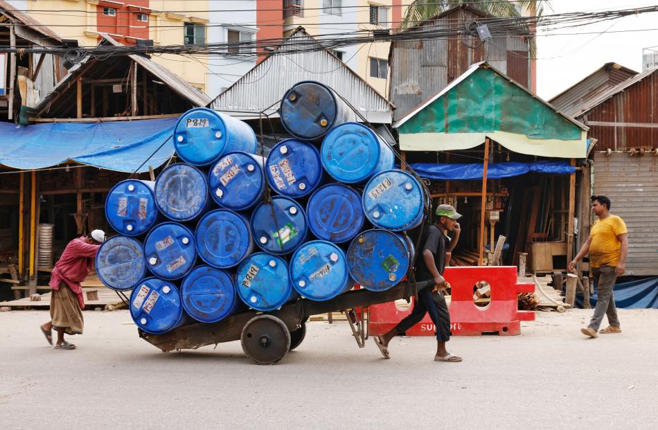 Bangladeshi labourers move a cart with drum containers in Dhaka, Bangladesh.