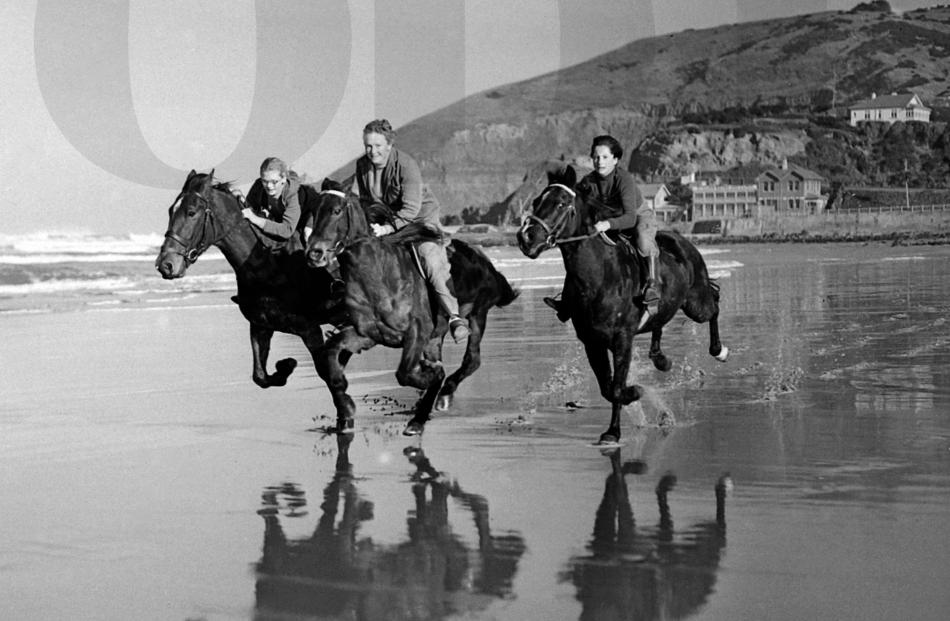 Three young riders are mirrored in the wet sand as they gallop along the beach at St Clair on a...