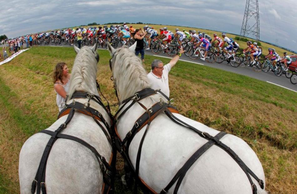 A pack of riders cycles past spectators with horses during the fifth stage of the 99th Tour de...