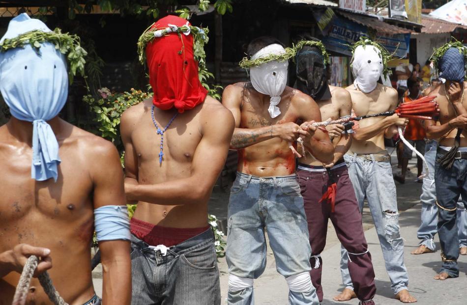 Hooded barefoot penitents perform self-flagellation to atone for their sins in San Fernando,...